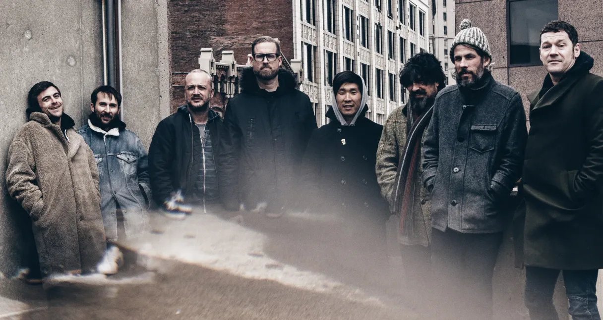 Image of eight men wearing coats in a city.
