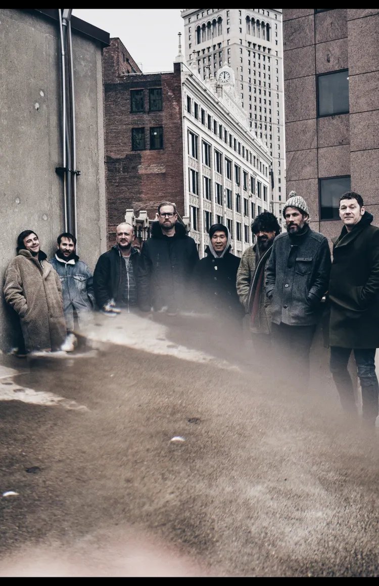 Image of eight men wearing coats in a city.