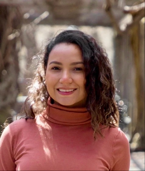 Curly hair woman wearing a coral turtleneck sweater.