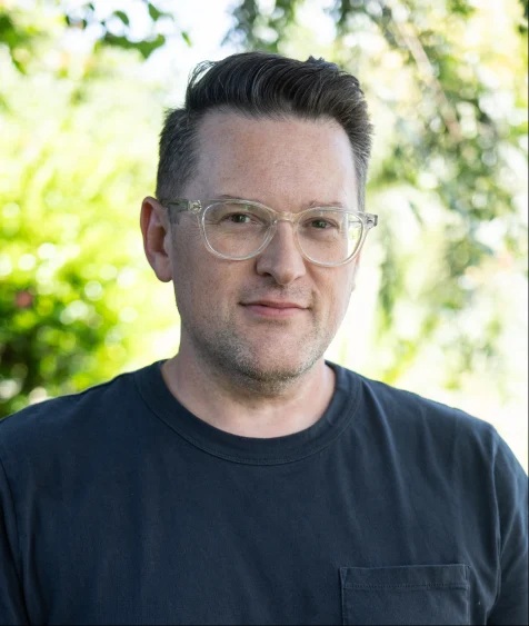 Portrait of a man wearing glasses and grey shirt.
