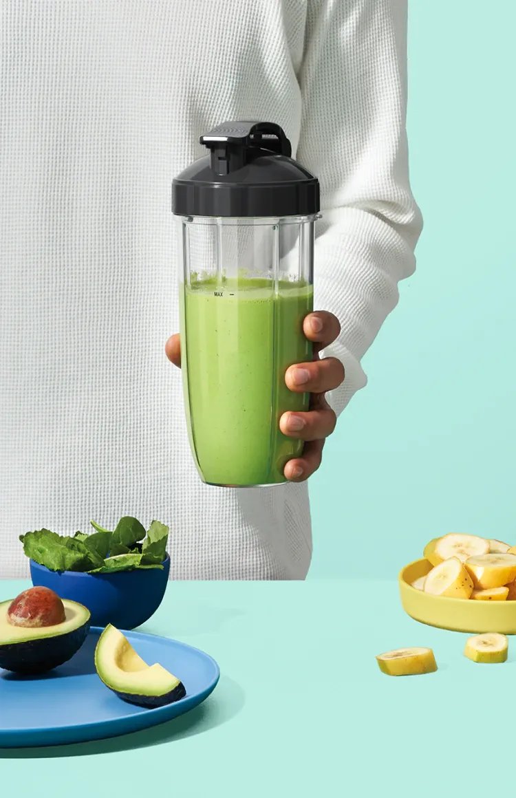 Image of a man holding a nutribullet with green smoothie on a mint background.