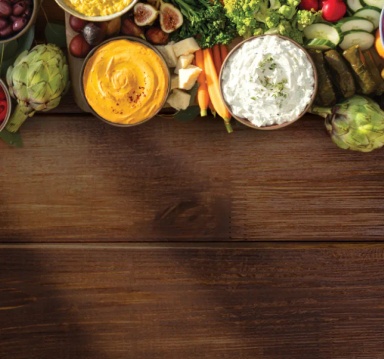 nourish-bg-mobile.webp Vegetables and spreads on wooden surface.