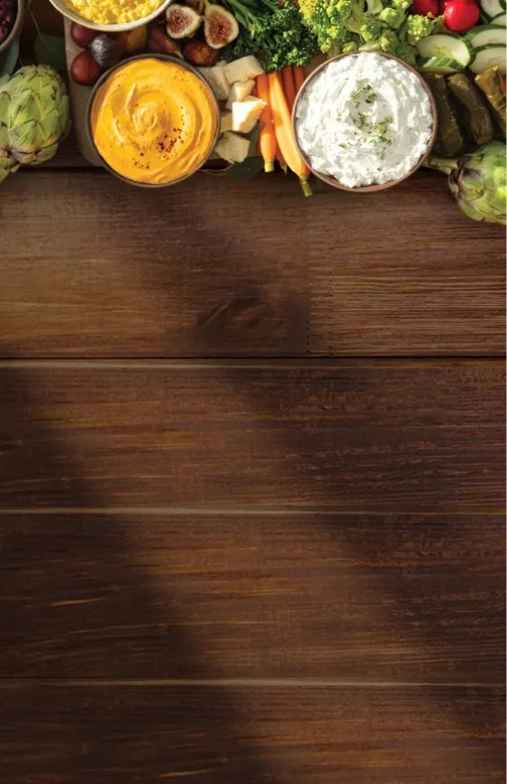 nourish-cardbg-desktop.webp Large array of vegetables and spreads on wooden surface.