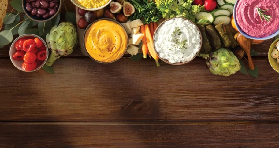 nourish-cardbg-mobile.webp Large array of vegetables and spreads on wooden surface.