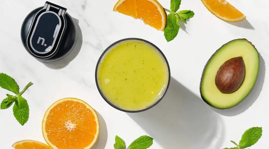 nourish-carousel-bg.webp Oranges and avocado on marble surface with green smoothie.